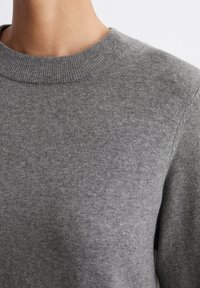 Maglione grigio lavorato a maglia con scollo rotondo, presentante una texture morbida e dettagli senza cuciture sulle spalle. Vista ravvicinata che mette in risalto la finitura del tessuto.