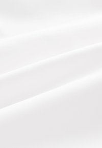 Tissu blanc lisse avec des plis subtils créant des ombres douces et des reflets sur toute la surface.