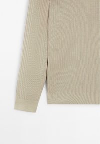 Light beige ribbed knit sweater with long sleeves, featuring a textured design and a straight hem. Soft, stretchy fabric for comfort.