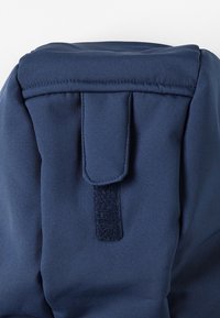 Marineblå stofrygsæk med toplukning og klap. Har en velcro-strop, glat tekstur og forstærkede sømdetaljer.