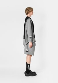 Sudadera gris con acentos negros, combinada con pantalones cortos grises y zuecos negros texturizados. Calcetines negros con letras blancas completan el look.
