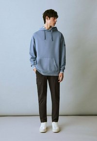 Hanorac din bumbac de culoare albastru deschis, cu buzunar tip kangaroo, asortat cu pantaloni cargo negri. Pantofi sport albi completează ținuta. Design simplu, modern.
