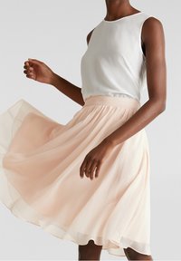 Lichtgewicht, mouwloze blouse in crème met een ronde halslijn, gecombineerd met een vloeiende, lichtroze rok met een geplooide tailleband.