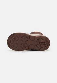 Bota marrón impermeable con suela de goma texturizada, que presenta un patrón de zigzag y un logotipo de marca visible. La parte superior está hecha de material duradero.