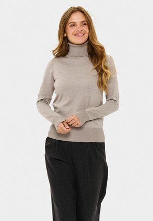 Beige Rollkragenpullover mit einem gerippten Kragen und Bündchen, aus weichem Stoff, kombiniert mit lockeren schwarzen Hosen, vor einem schlichten Hintergrund stehend.