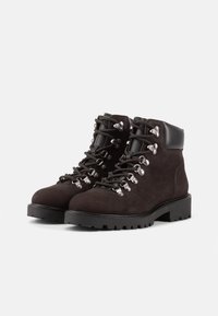 Ciemnobrązowe zamszowe buty trekkingowe z metalowymi oczkami, czarnymi skórzanymi akcentami na kostce i wytrzymałymi gumowymi podeszwami. Oferują sznurowany fason.