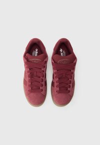 Bordinės spalvos sportbačiai su zomšiniu viršumi, paminkštu apykakle ir tekstūruotomis raištelėmis. Turi gumines padas ir iškilų logotipą ant liežuvėlio.