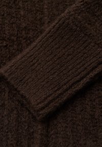 Primo piano di un tessuto lavorato a maglia marrone scuro con dettaglio di polsino a costine, che mostra spesse fibre di lana intrecciata e texturizzata.