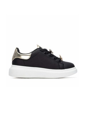 Zapatilla deportiva negra de corte bajo con detalle metálico dorado en el talón, cordones negros con adornos decorativos y suela blanca gruesa.