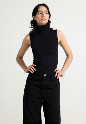 Zwarte geribbelde mouwloze coltrui gecombineerd met zwarte high-waisted jeans. De stof is glad met een getailleerd ontwerp en minimale details.
