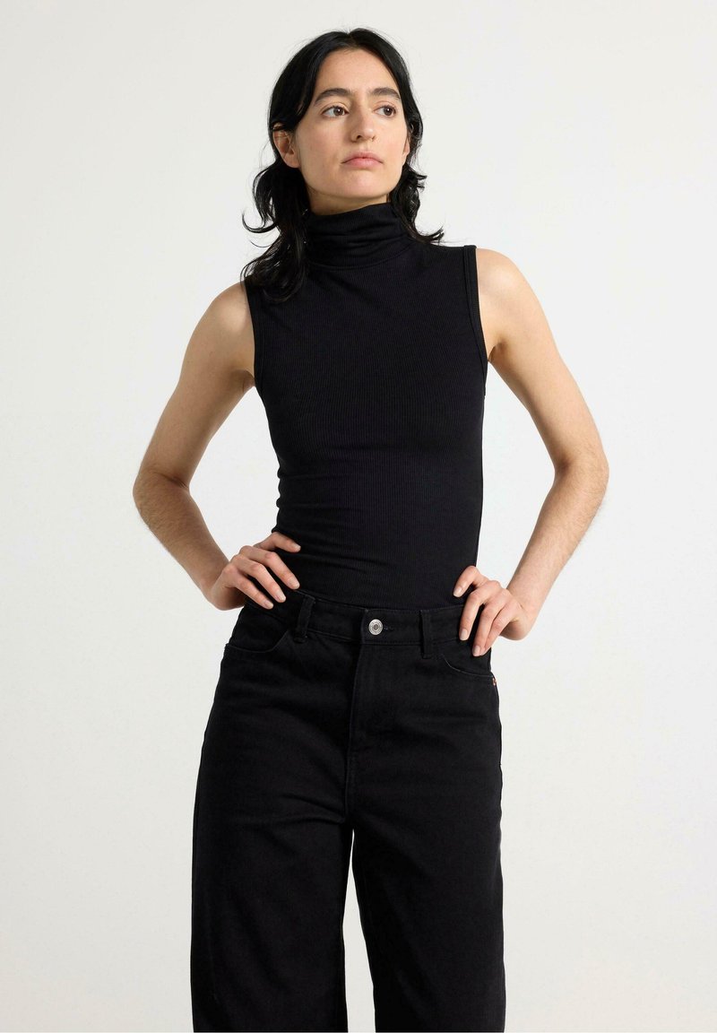 Sort ribbet ærmeløs turtleneck-top samlet med højhvide sorte jeans. Stoffet er glat med et tætsiddende design og minimal detaljer.