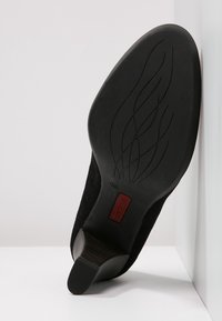 Černá semišová vysoká bota na podpatku s zakřivenou špičkou, podpatkem s dřevěným akcentem a texturovanou gumovou podrážkou s vlnkovými vzory a drobným červeným logem.