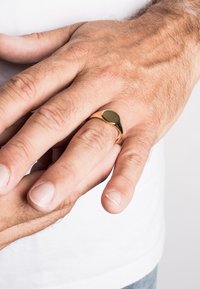 Gouden ring met een gladde, ovale zwarte steeninstelling, gedragen aan een hand met kort, licht haar en schone, natuurlijke nagels.