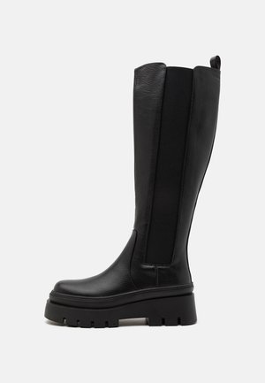 Black knee-high boot made of smooth leather with elastic side panels, chunky platform sole, and ribbed texture on the base.