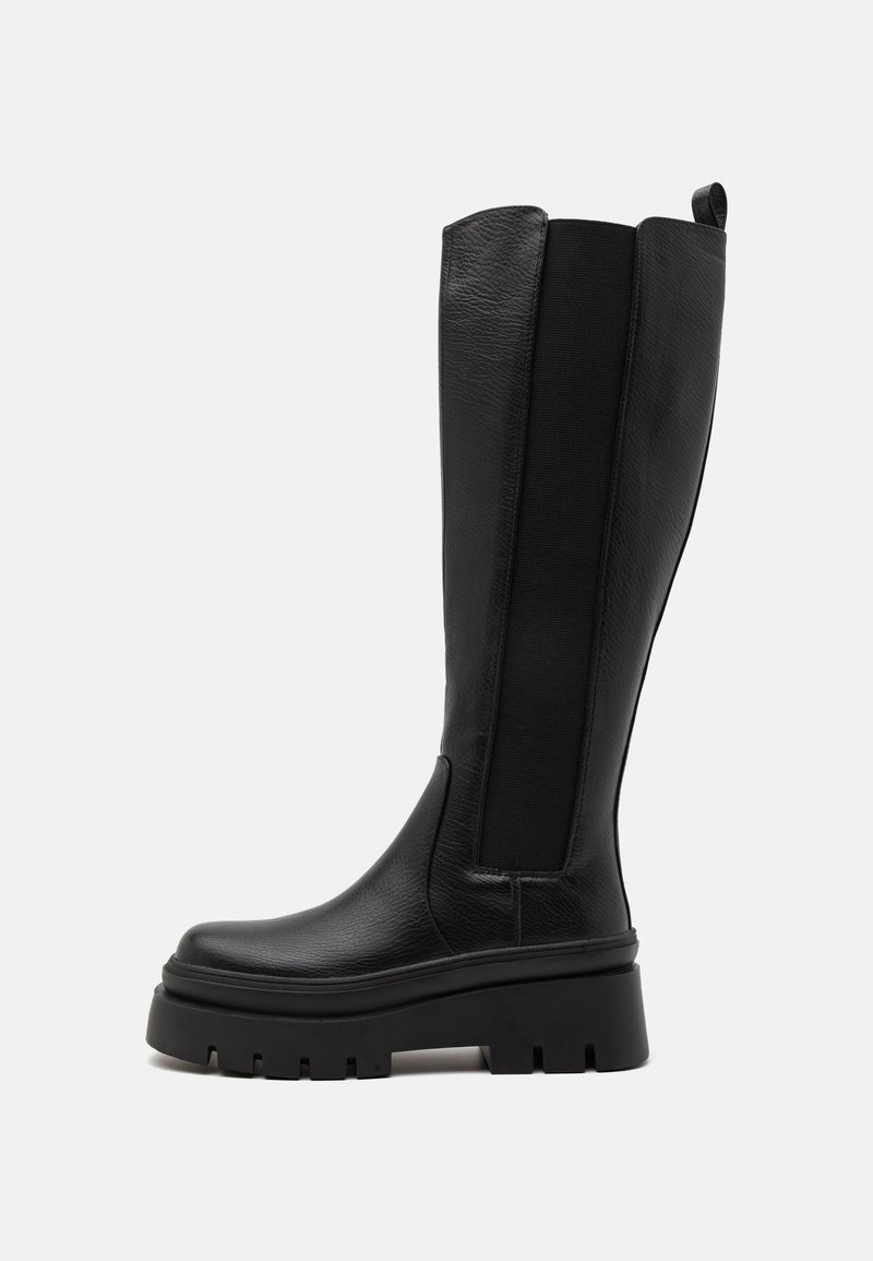 Black knee-high boot made of smooth leather with elastic side panels, chunky platform sole, and ribbed texture on the base.