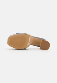 Chaussure à talon haut en textile gris avec une semelle lisse et texturée, un talon en caoutchouc et un détail de logo en relief sur la semelle.
