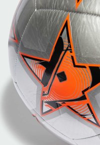 Palla da calcio argento con un design a stelle nere e accenti arancioni, superficie liscia e cuciture ben definite lungo le giunture.