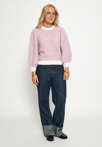Rosa och vit mönstrad stickad tröja med ballongärmar, kombinerad med mörkblå vida jeans med uppvikta fållar och svarta skor.