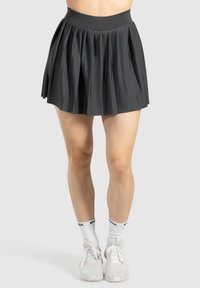 Zwarte geplooide rok met een hoge tailleband, gemaakt van een textuurstof. Witte sportschoenen en sokken maken de outfit compleet. Eenvoudig, modern ontwerp.