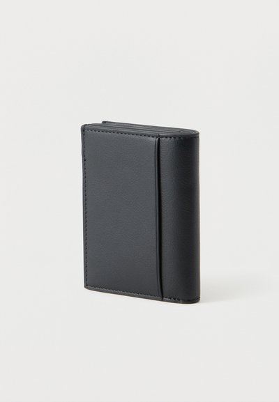 Portefeuille bifold en cuir noir debout sur un fond blanc uni, montrant l'extérieur texturé et les bords cousus.