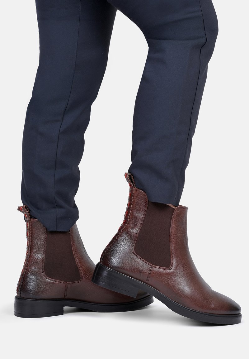 Brązowe skórzane botki typu chelsea z elastycznymi panelami bocznymi i teksturowanym wykończeniem, z kontrastującym przeszyciem na tylnej części oraz niskim obcasem.