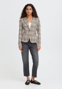 Blazer v světle béžovém kostkovaném designu, přiléhavý střih s jedním knoflíkem. Spárován s tmavě šedými džínami a plochými černými botami.