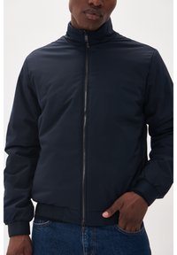 Giacca bomber navy realizzata in tessuto liscio e resistente all'acqua. Presenta un colletto alto, chiusura frontale con zip e polsini e fondo a costine.