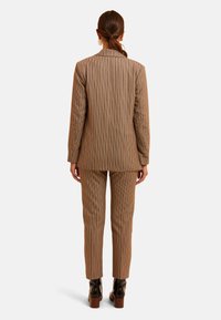 Chaqueta de traje marrón a cuadros y pantalones ajustados, con solapas de muesca y piernas ajustadas. La tela tiene una textura suave con patrones sutiles.
