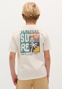 Cremefarbenes Baumwoll-T-Shirt mit einem grafischen Druck auf der Rückseite, der Text, einen Schädel, eine Palme und bunte geometrische Formen zeigt.