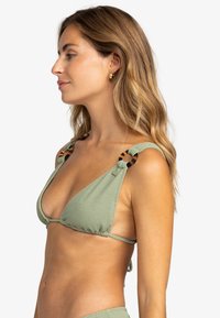 Top de bikini triangular en tejido texturizado de color verde claro, con detalle de carey en las correas de los hombros. Lazos ajustables en la parte trasera.
