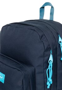 Zaino navy con cerniere blu chiaro, tessuto texturizzato e manico superiore a righe. Presenta più scomparti e un'etichetta con il logo.