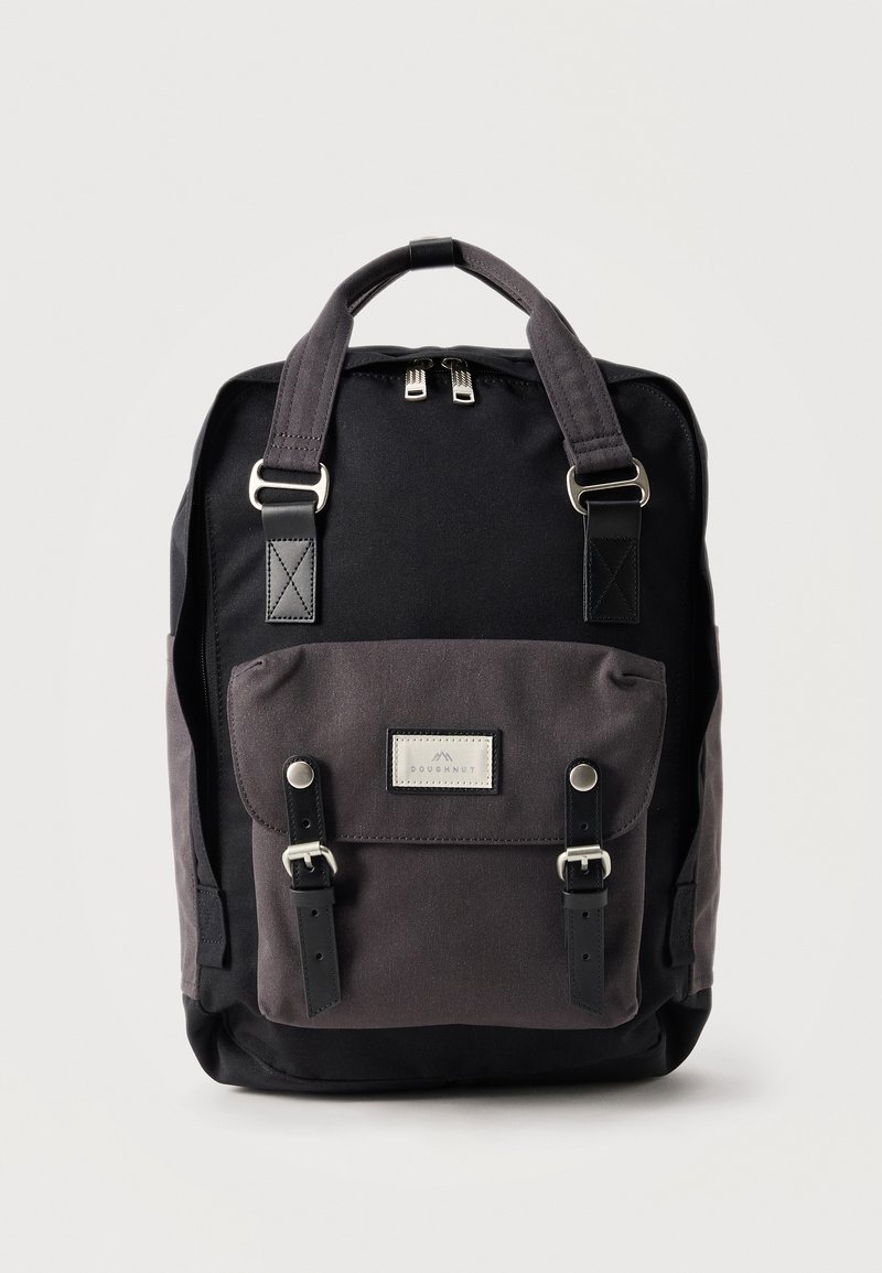 Μαύρο και σκούρο γκρι σακίδιο πλάτης με δύο λαβές στην κορυφή, μπροστινή τσέπη με καπάκι ασφαλισμένη με δύο αγκράφες και διπλό φερμουάρ στην πάνω πλευρά.