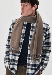 Beige gyapjú sál, rojtos végekkel, a nyak köré tekerve, kockás inggel viselve kék, fehér és barna árnyalatokban.