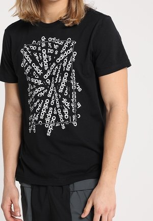 Schwarzes Baumwoll-T-Shirt mit einem auffälligen Grafikdesign, das wiederholt weißen "adidas"-Text in verschiedenen Ausrichtungen und einem rechteckigen Rahmen zeigt.