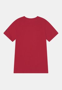 Camiseta de algodón roja con mangas cortas y cuello redondo. Presenta un logo en la manga izquierda. Textura suave y dobladillo recto.