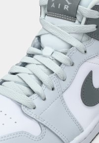 Baskets Nike grises et blanches en suède et cuir, avec une languette rembourrée, des lacets plats, un bout rond et un swoosh prominent.