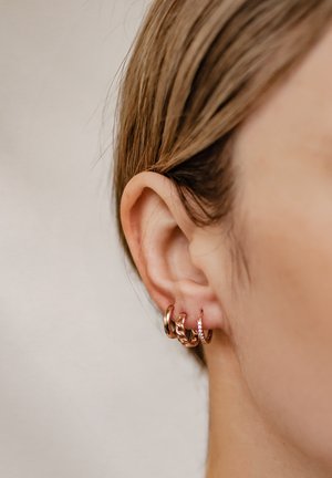 Vier Creolen in einer Mischung aus Gold und Roségold, mit unterschiedlichen Designs: glatt, verdreht und mit kleinen Edelsteinen verziert.