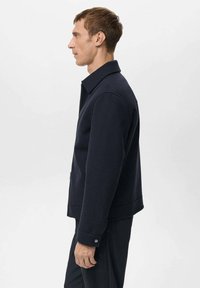 Granatowa polarowa kurtka z usztywnionym kołnierzem, bocznymi kieszeniami i mankietami zapinanymi na guziki. Prosty krój o fakturowanej powierzchni. Minimalistyczny design.