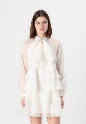 Robe blanche à couches avec un tissu transparent, des volants, de longues manches translucides et un détail de décolleté avec un nœud. Texture lisse dans l'ensemble.