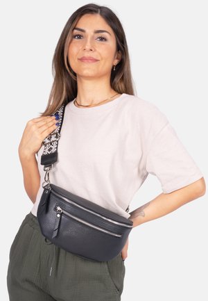 Sac en cuir noir à bandoulière avec deux compartiments zippés en argent, surface texturée et une sangle à motif avec des accents noir et blanc.