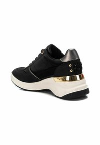 Zapatilla deportiva negra con parte superior texturizada, detalles metálicos, talón dorado y una suela blanca gruesa, que cuenta con cordones y costuras decorativas.