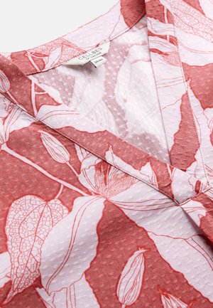 V-udskåret beklædningsgenstand med stof i pink og rød botanisk tryk, der viser sarte blade og blomsterdesigns, tekstureret med små forhøjede prikker.