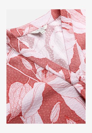 V-Ausschnitt Kleidungsstück mit pink-rotem botanischem Printstoff, der zarte Blatt- und Blumendesigns zeigt, strukturiert mit kleinen erhabenen Punkten.