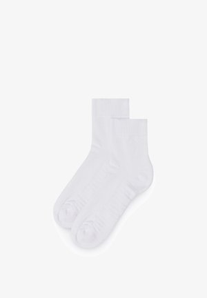 Paire de chaussettes basses blanches unies avec bords côtelés, présentées à plat sur un fond blanc.