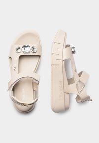 Sandali beige con suola spessa, dotati di tre gemme trasparenti sulla cinghia. Realizzati in materiale liscio con un design semplice e fibbia regolabile.
