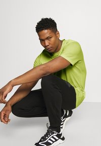 T-shirt verde a maniche corte abbinato a pantaloni joggers neri e sneaker bianco e nero. Tessuto morbido e vestibilità rilassata, con un logo del brand discreto.