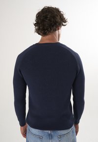 Granatowy sweter wykonany na drutach z prążkowaną teksturą, okrągłym dekoltem i długimi rękawami, z raglanowymi szwami na ramionach oraz dopasowanym krojem.