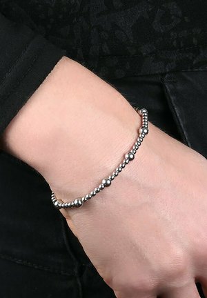 Braccialetto in argento con perle alternanti lisce e texturizzate, posizionato su un polso nudo, con una lucentezza sottile e un design flessibile.