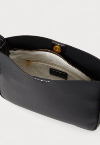 Borsa a mano in pelle nera con una texture liscia, dotata di una tasca interna con zip e hardware dorato. Cuciture bianche accentuano il bordo superiore.