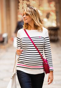 Gestreiftes Langarm-Oberteil in Weiß, Schwarz und Pink mit einem Herzdetails. Kombiniert mit dunklen Jeans und einer kleinen rosa Umhängetasche.